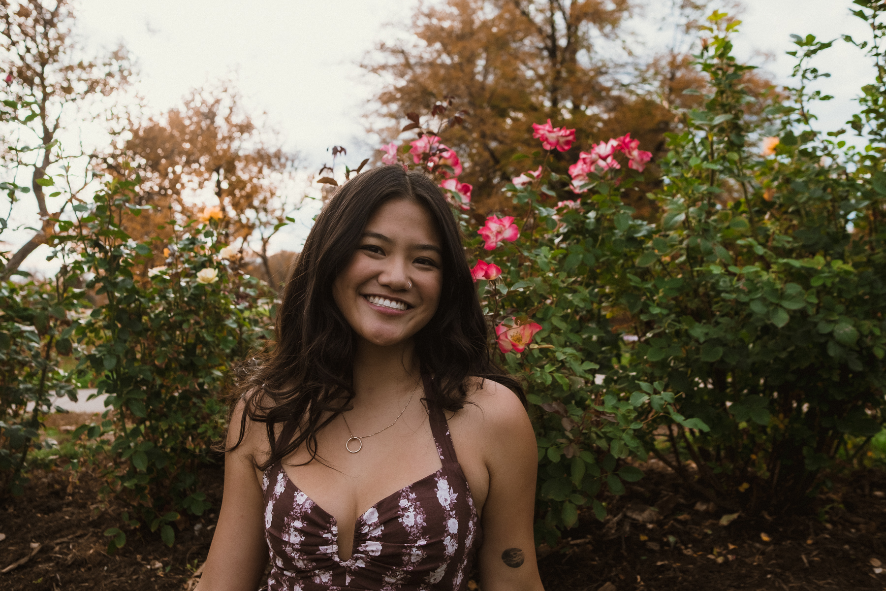 Izzy smiling in front of pink roses in an autumn garden
